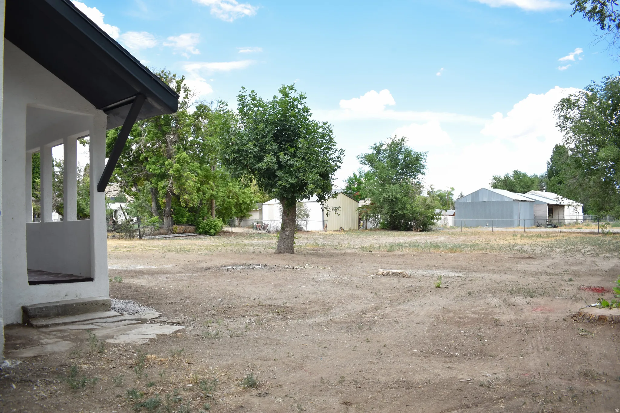 Large property grounds featuring a concrete slab porch, mature tree, and multiple outbuildings