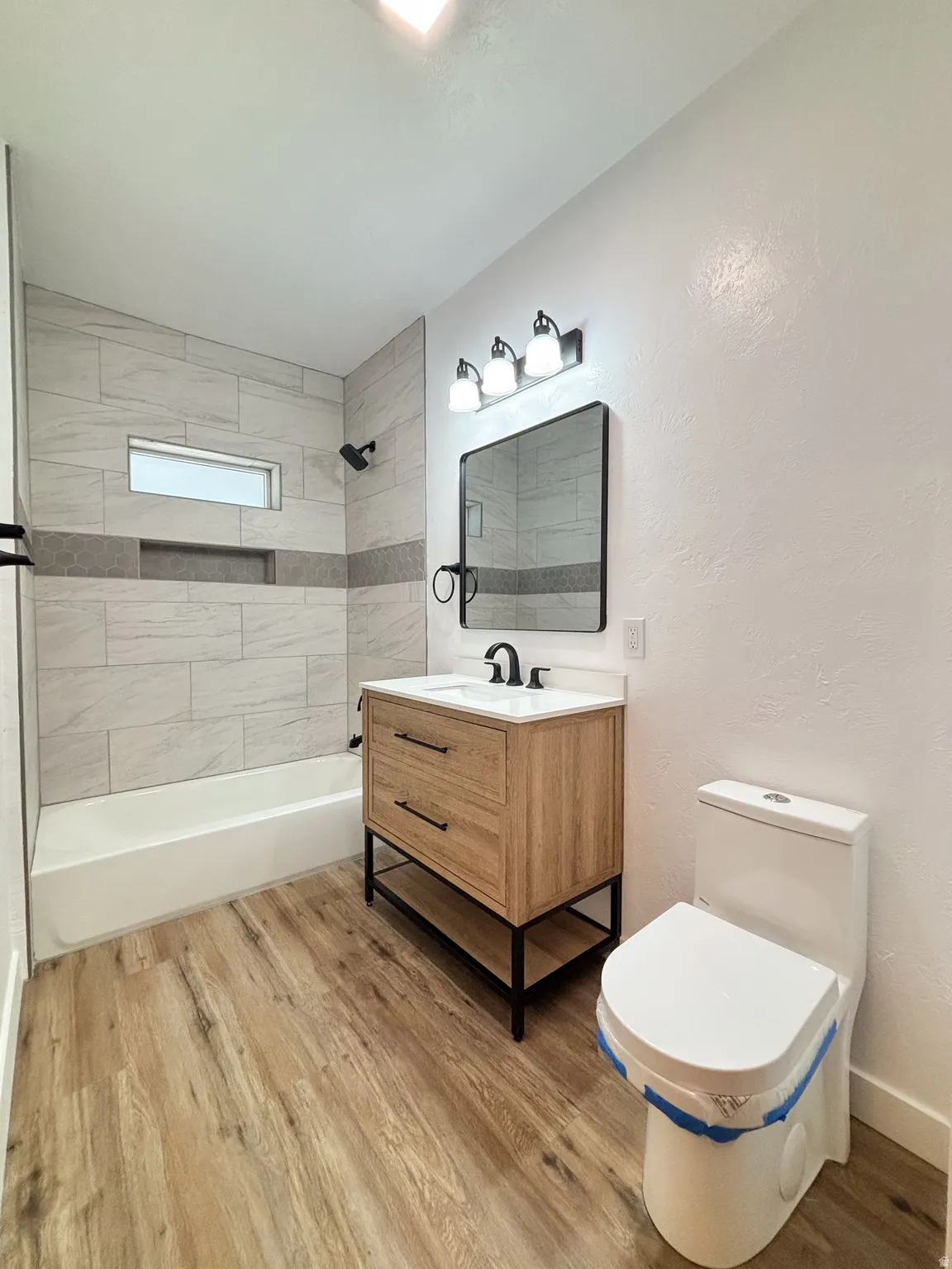 Modern bathroom featuring wood-finish flooring and a contemporary vanity with black hardware