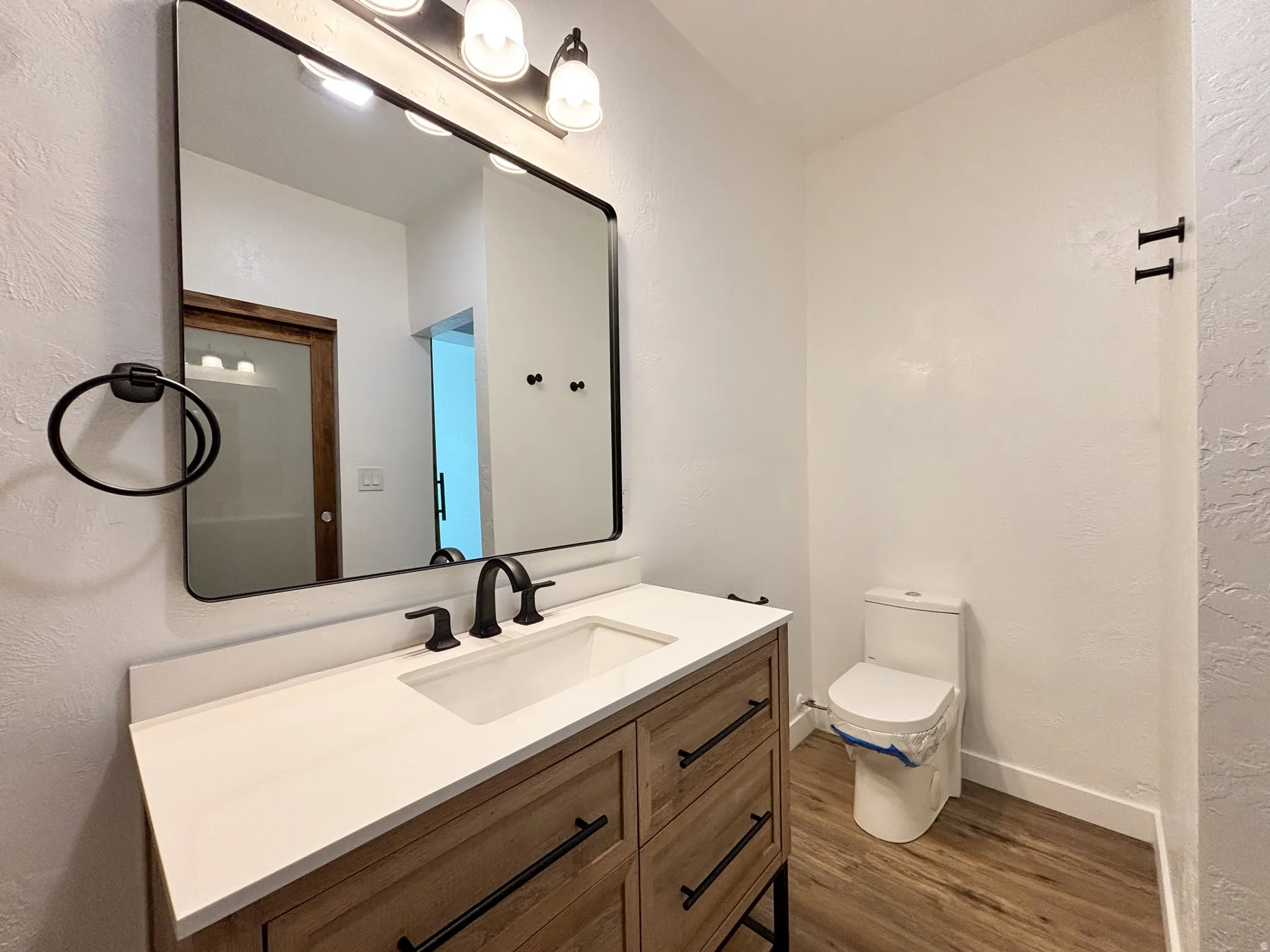 Bathroom featuring a wood-finish vanity with a white countertop, an integrated rectangular sink, a matte black faucet, and a large framed mirror