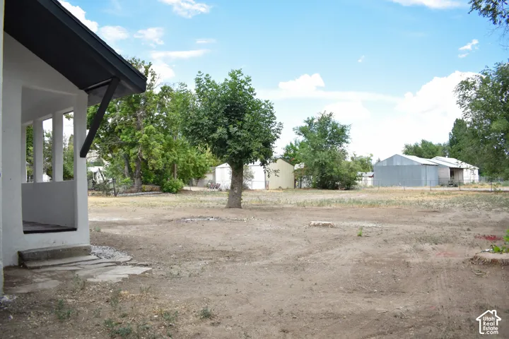 Large property grounds featuring a concrete slab porch, mature tree, and multiple outbuildings