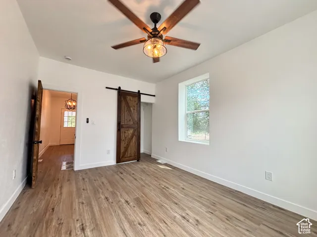 Spacious interior room featuring wood-finish flooring, a ceiling fan with light fixture, and a single window