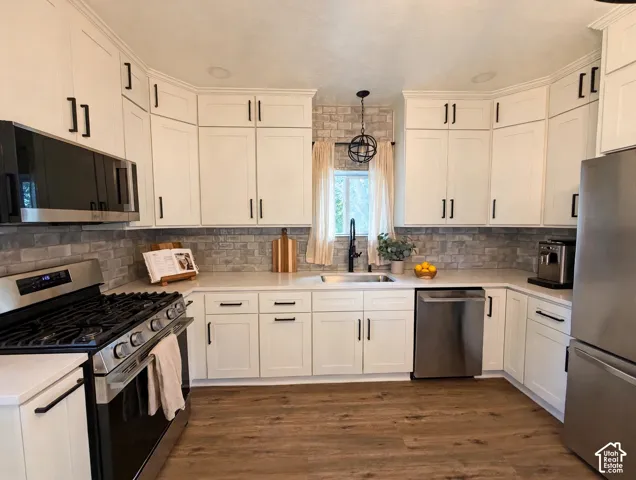 Kitchen featuring white shaker-style cabinetry with matte black hardware, stone-finish backsplash, stainless steel appliances, and wood-finish flooring