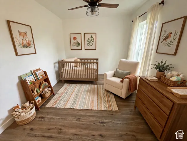 Bedroom featuring wood-finish flooring, a ceiling fan with a cage-style light fixture, and windows equipped with neutral-toned curtains