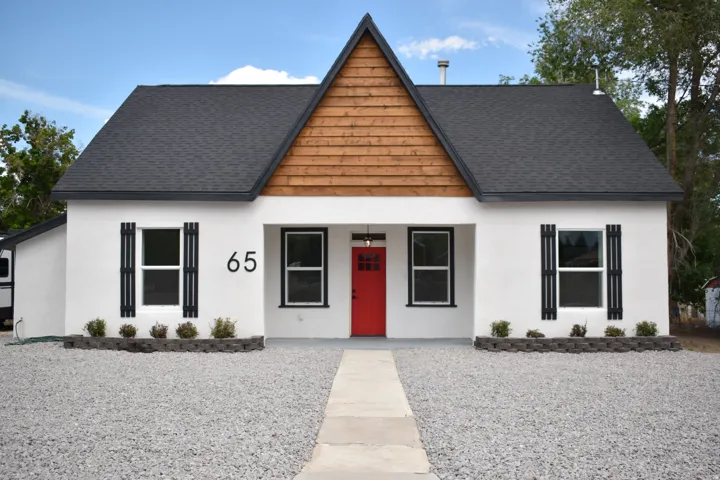White stucco exterior with a prominent wooden gable accent, dark shingle roof, and striking red entry door