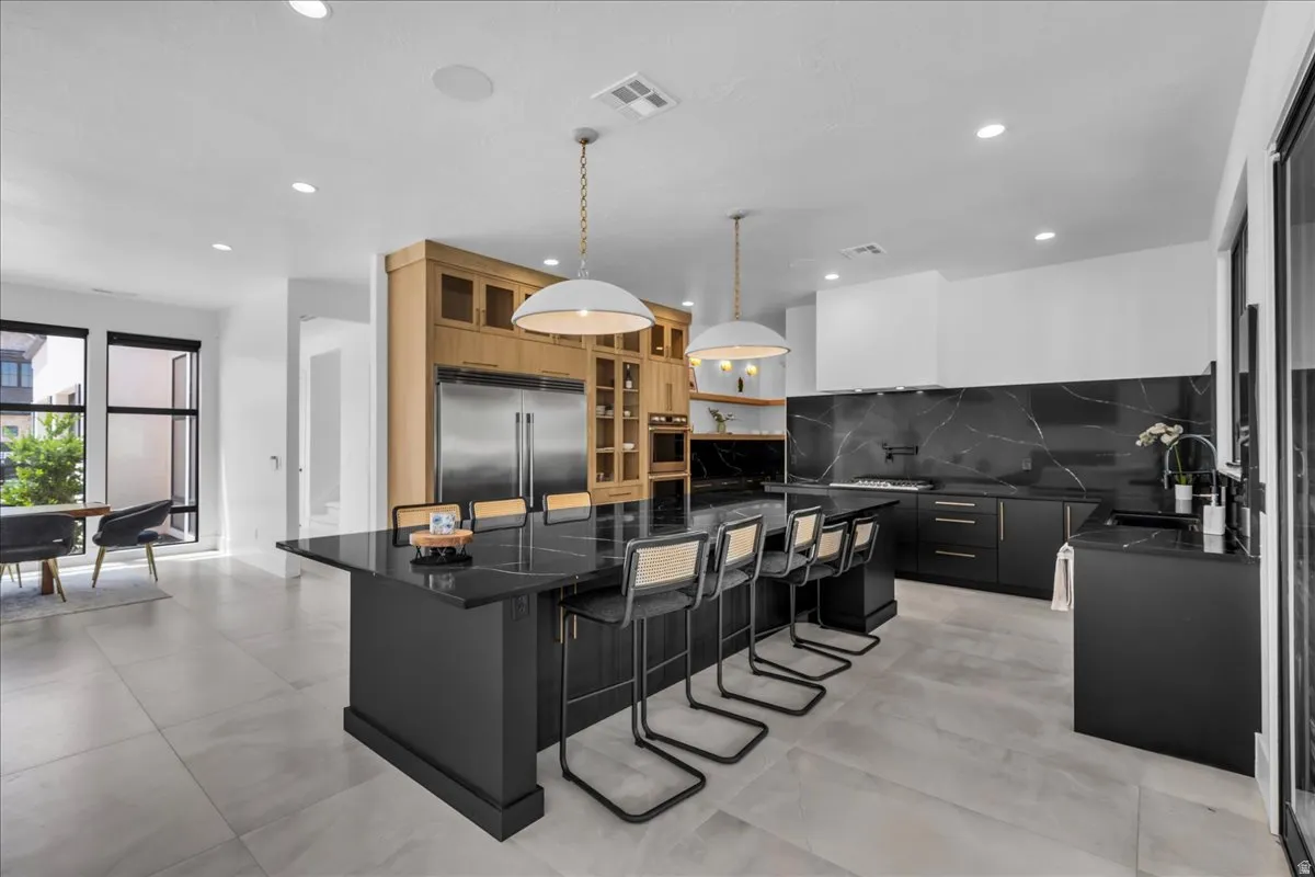 Spacious kitchen featuring a large black island with seating, dark cabinetry, and integrated stainless steel appliances