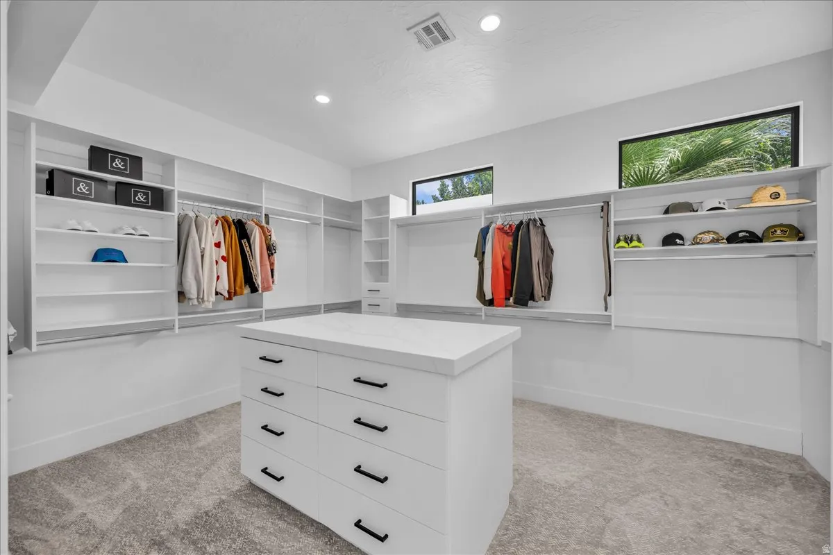 Spacious closet design featuring a central dresser island with a light-toned countertop, extensive built-in shelving, multiple hanging rods, and integrated recessed lighting