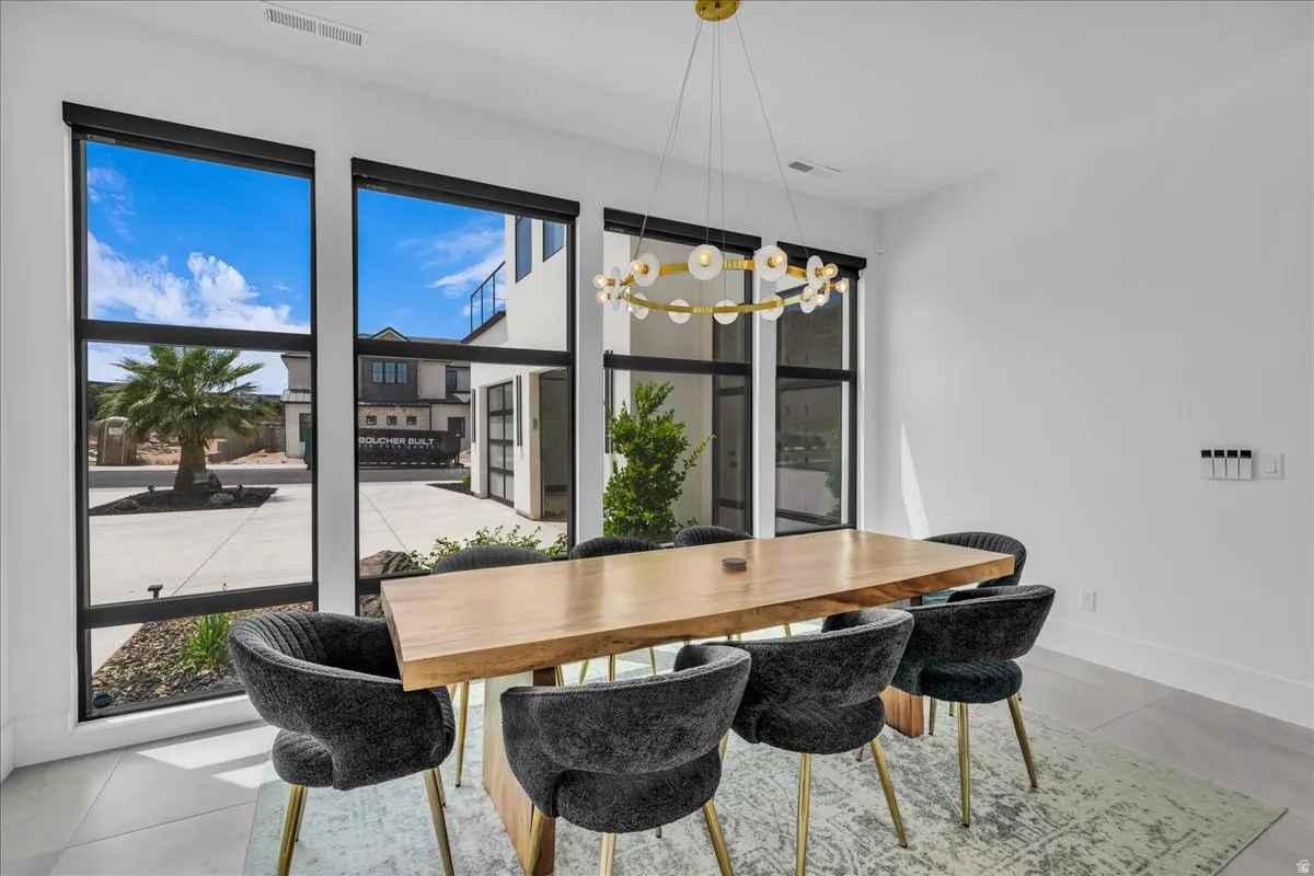 Dining area featuring a modern linear chandelier, floor-to-ceiling windows with black frames, and light-tone flooring