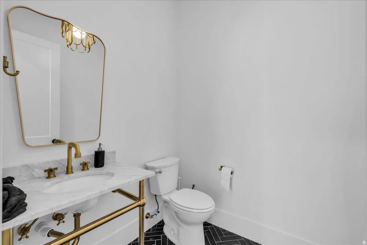 Powder room featuring a brass-framed mirror, brass vanity with a marble countertop, brass faucet, and black herringbone tile flooring