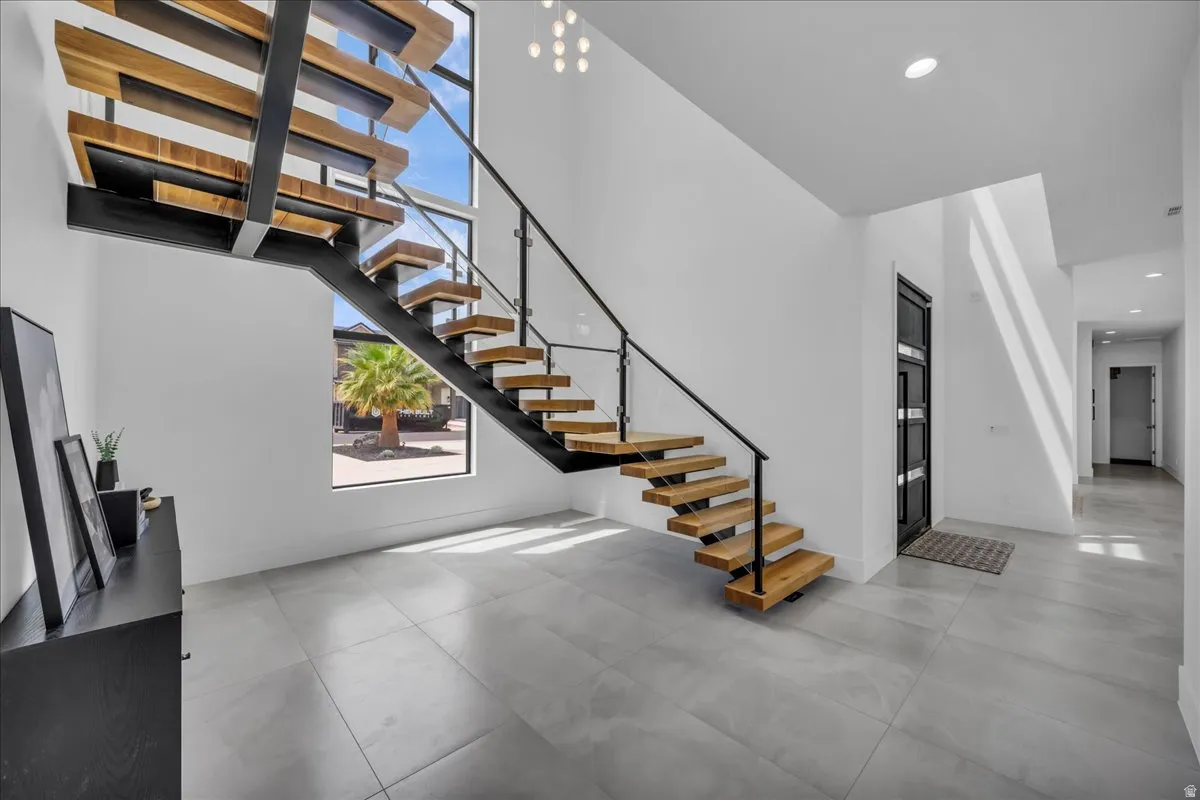 Open-concept entryway featuring a floating wood staircase with metal and glass railings, large format tile flooring, a multi-paneled entry door, and high ceilings with recessed lighting