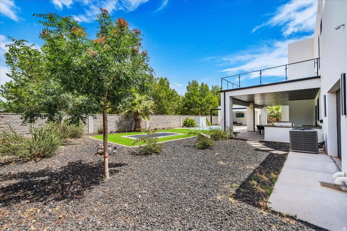 Expansive outdoor area featuring a modern covered patio with an outdoor kitchen, a second-story balcony with glass railings, a swimming pool, and a low-maintenance landscape with dark gravel and artificial turf
