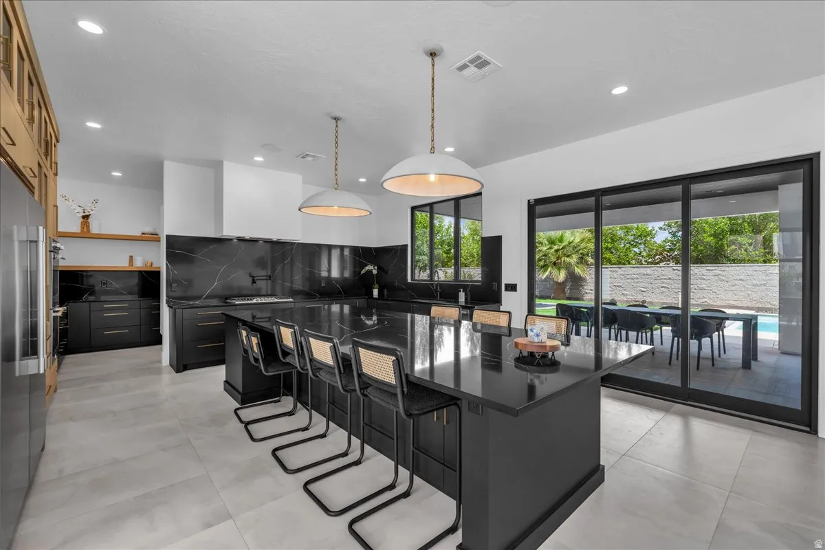 Modern kitchen featuring a large central island, black cabinetry, and dark countertop surfaces with a subtle vein pattern