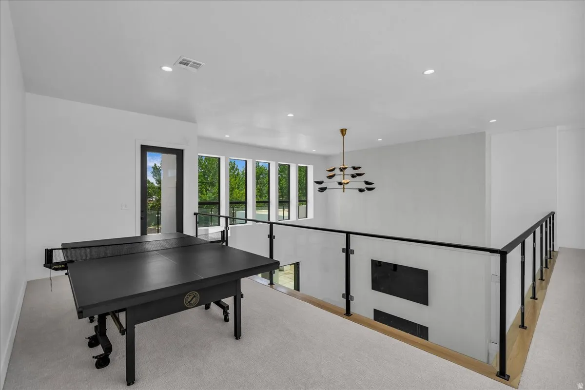 Open concept upper level featuring expansive windows, recessed lighting, a modern chandelier, and a glass panel railing system with black metal accents