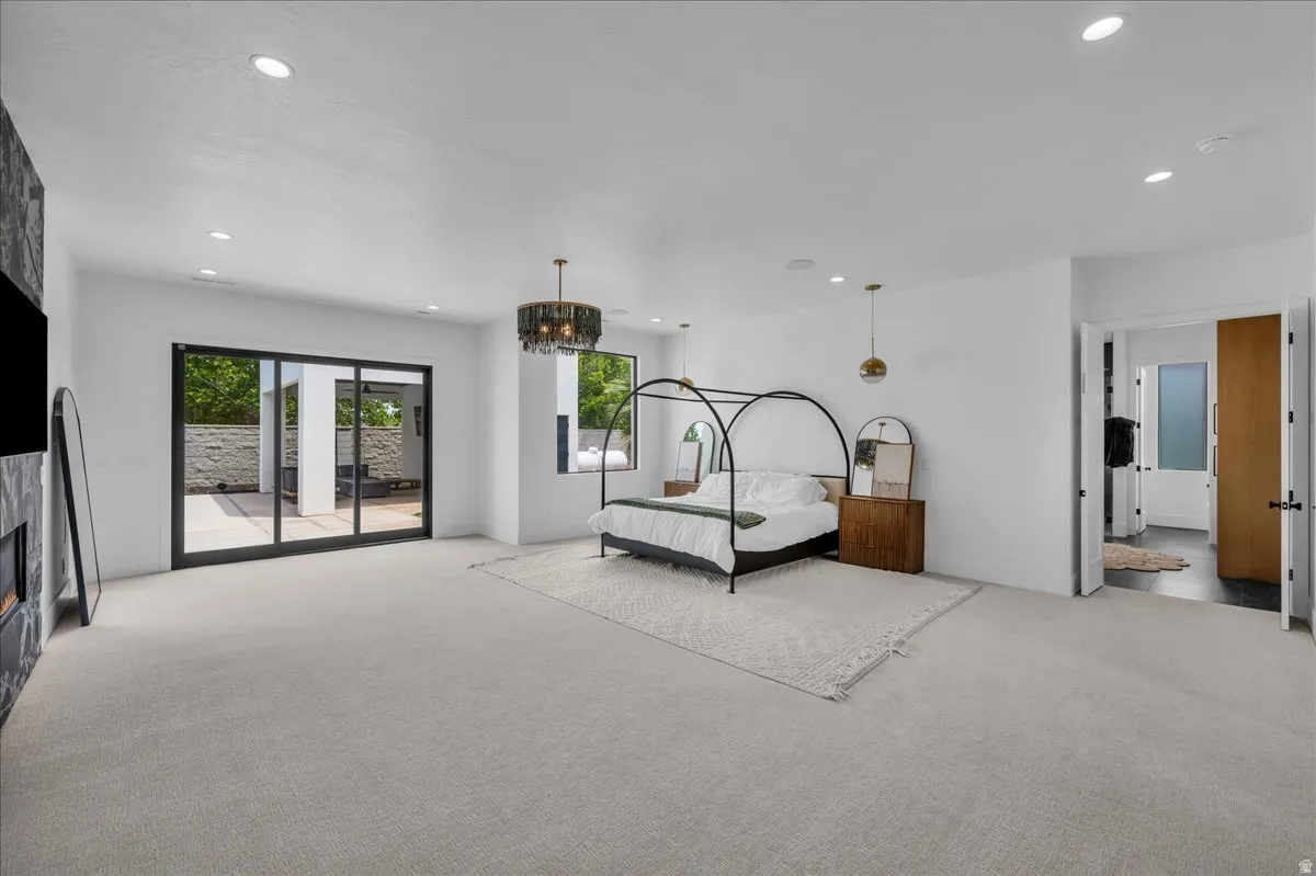 Spacious bedroom featuring light-colored carpeting, recessed lighting, and a dark stone-clad fireplace