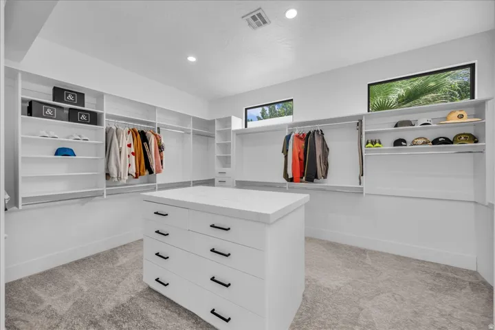 Spacious closet design featuring a central dresser island with a light-toned countertop, extensive built-in shelving, multiple hanging rods, and integrated recessed lighting