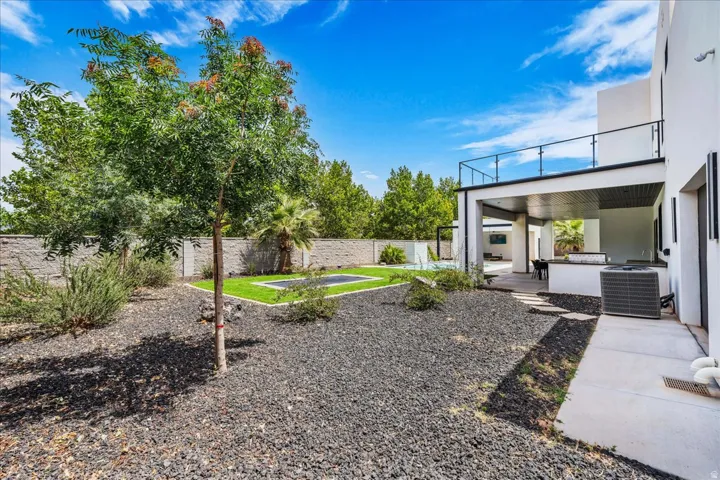 Expansive outdoor area featuring a modern covered patio with an outdoor kitchen, a second-story balcony with glass railings, a swimming pool, and a low-maintenance landscape with dark gravel and artificial turf