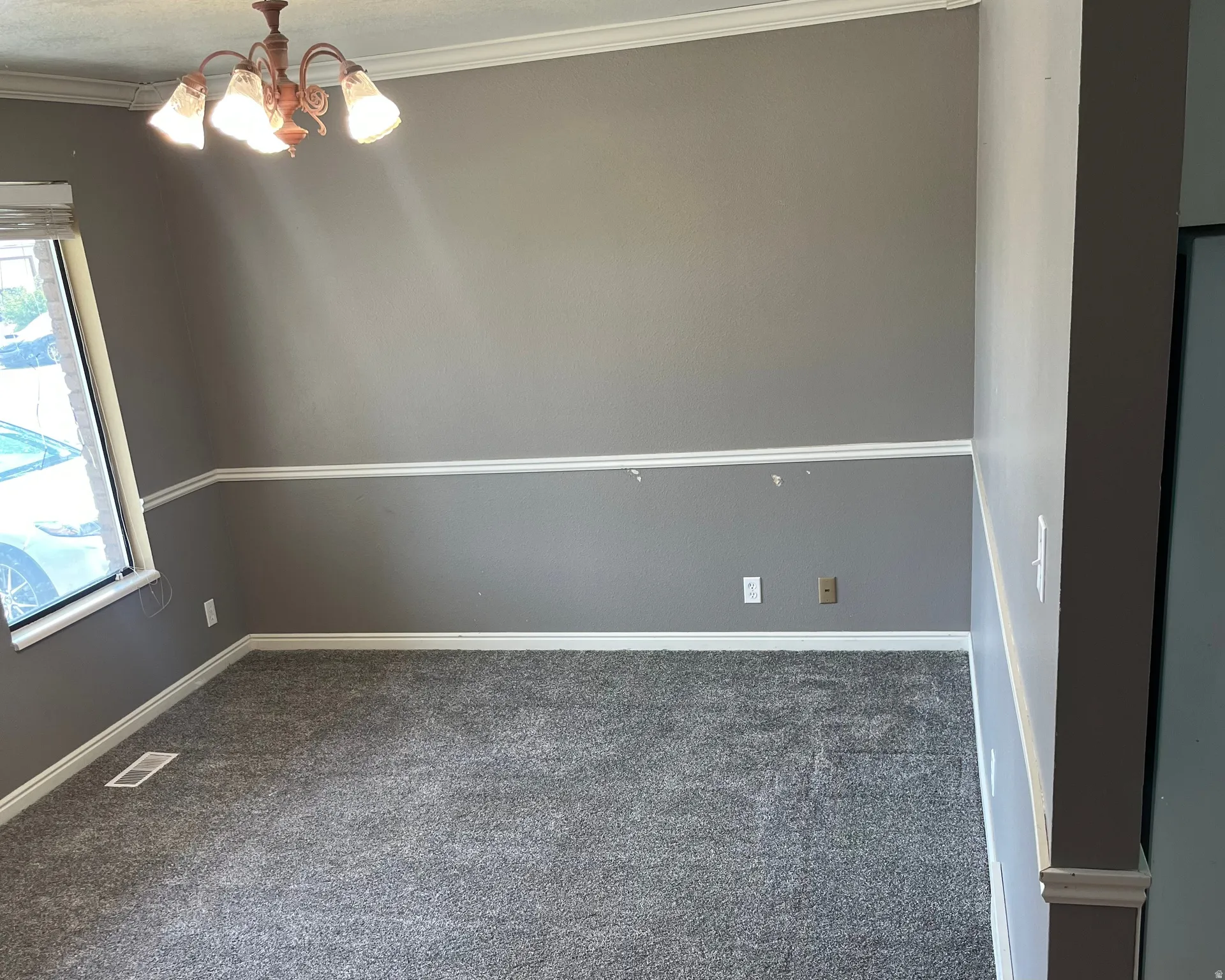 Carpeted living space featuring a window with blinds, a multi-light ceiling fixture, crown molding, chair rail molding, and baseboard trim