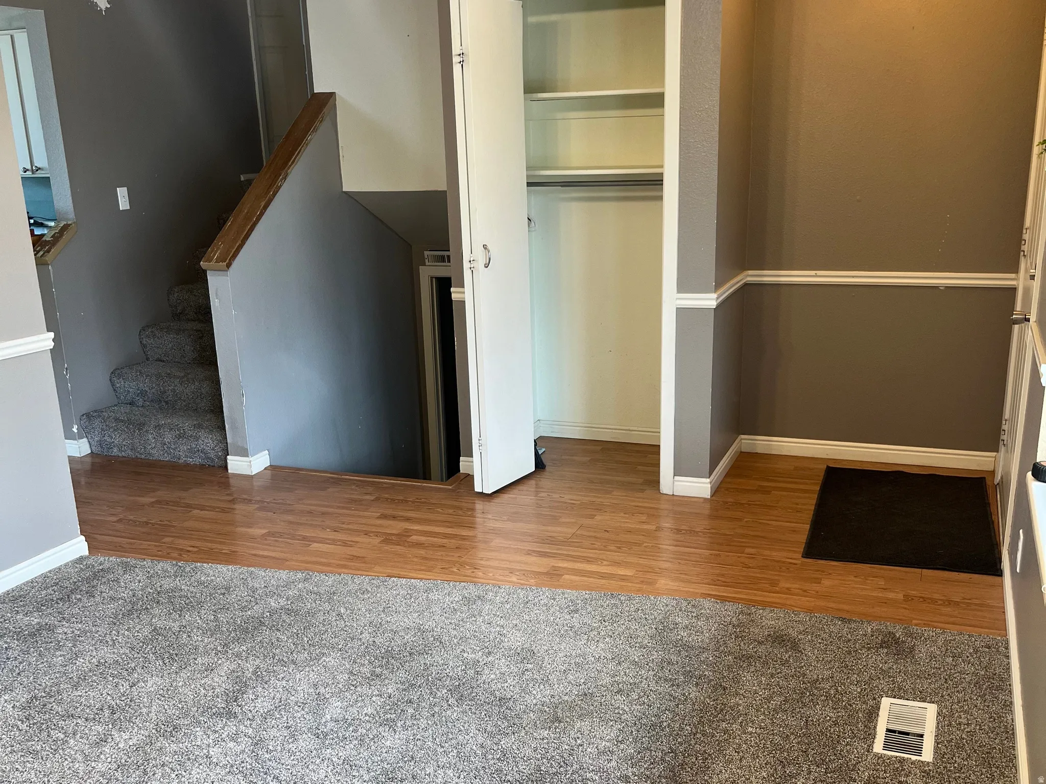 Entryway featuring wood-finish flooring, a carpeted staircase with wood handrail, and white baseboard and chair rail molding. Entry coat closet. Stairs that go up to the 2nd level, and stairs that go down to the basement.