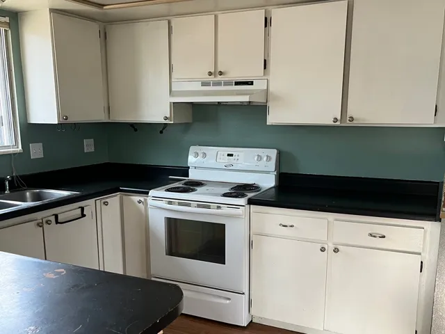 Kitchen featuring white cabinetry, dark countertops, a built-in range, and a double basin sink