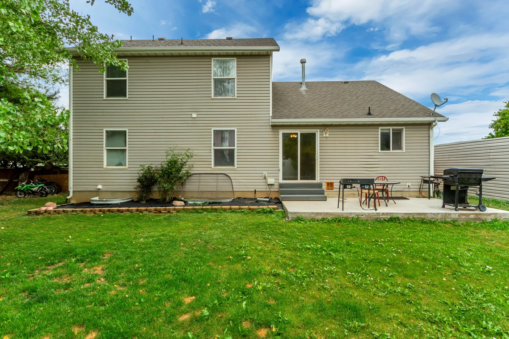 Rear exterior featuring beige siding, multiple windows, and a concrete patio