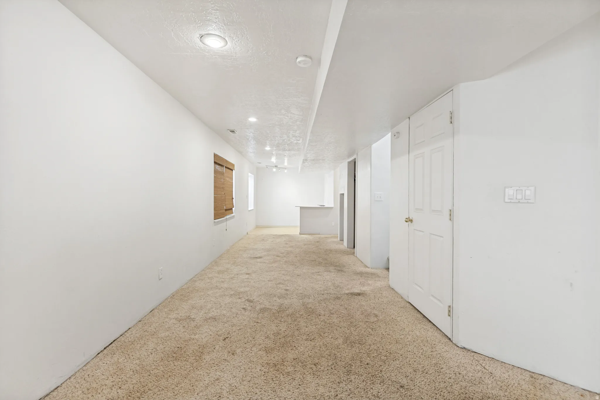 Spacious carpeted room featuring recessed lighting, a white door, and a built-in counter surface