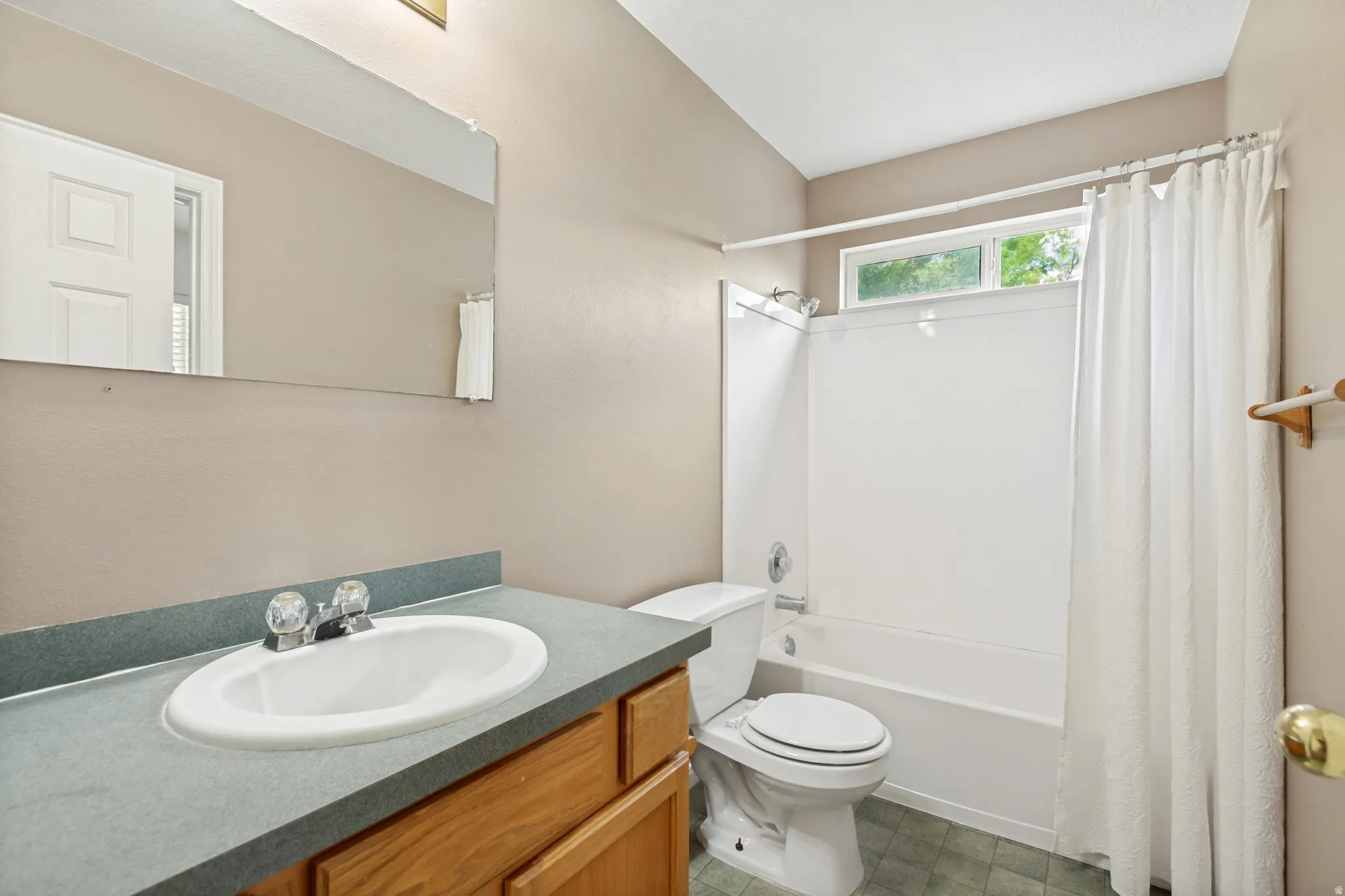 Bathroom featuring a vanity with a white oval sink and a gray countertop, a full bathtub with a shower, and a high window