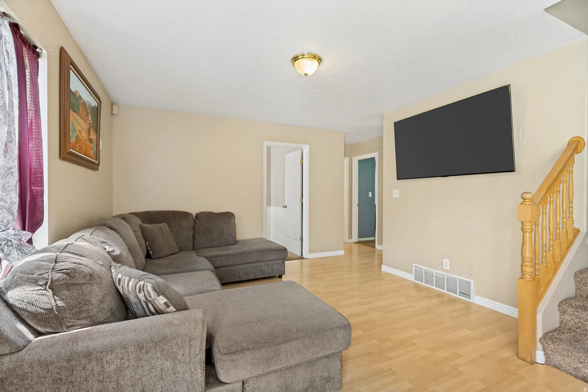 Spacious room featuring light wood-finish flooring, neutral wall tones, and a traditional brass flush-mount light fixture