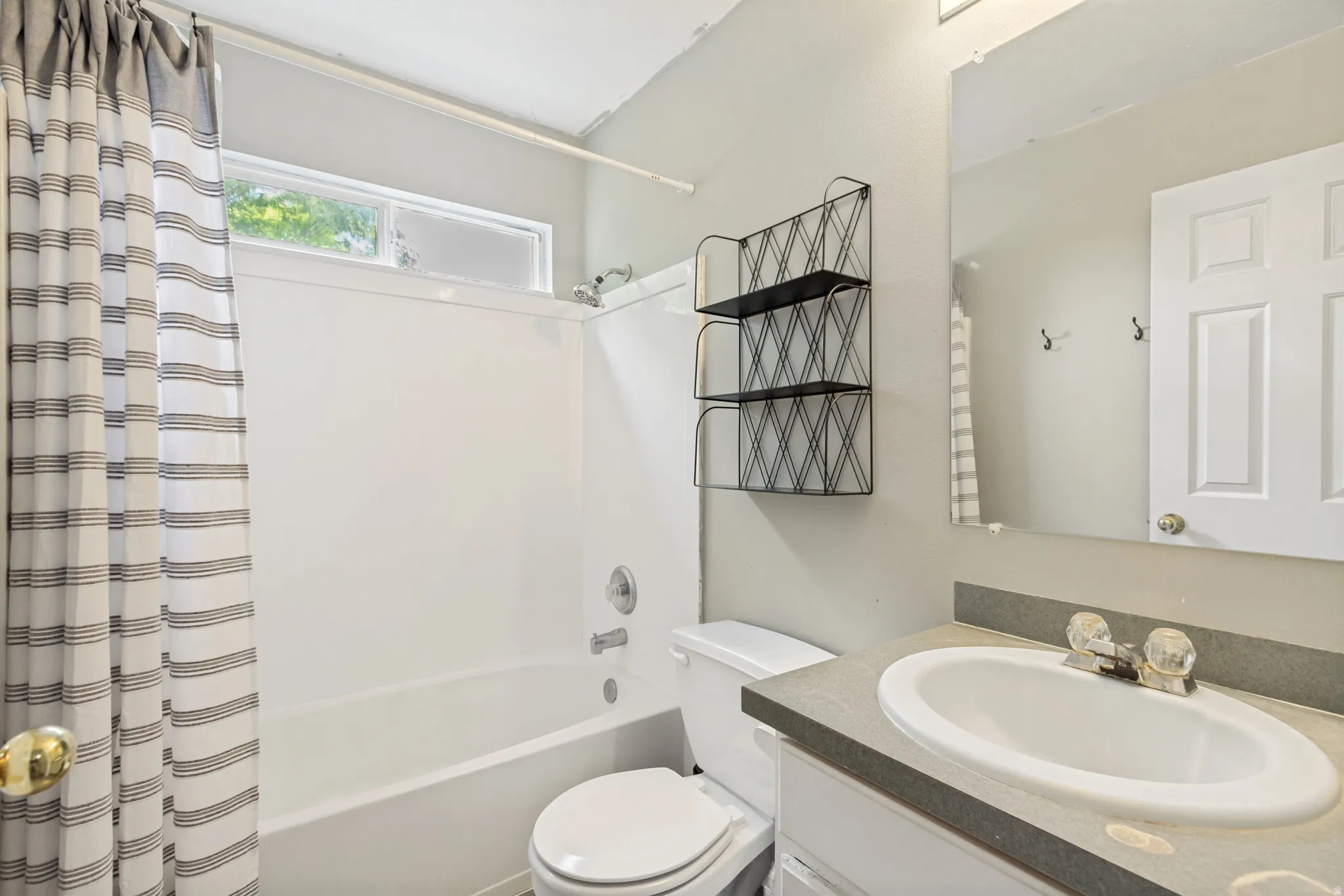 Bathroom featuring a white tub/shower combination with a transom window, a single vanity with a white basin and gray countertop, and a wall-mounted mirror