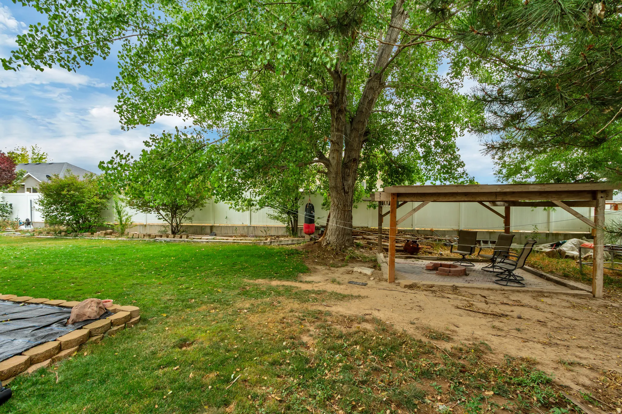 Spacious backyard featuring a covered patio structure, dedicated fire pit area with paver base, mature shade tree, and a manicured lawn