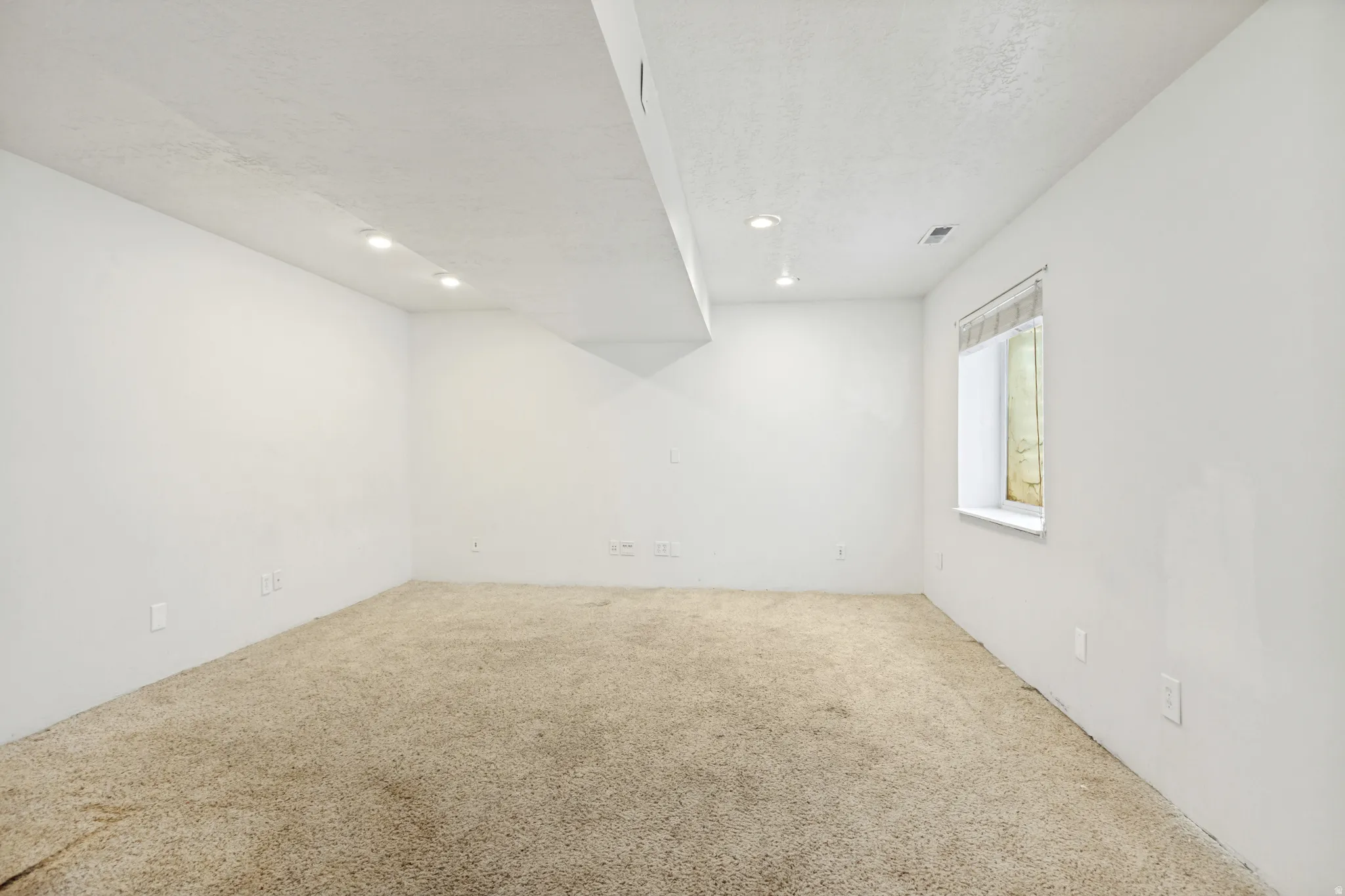 Spacious room featuring neutral carpeting, white painted walls, and recessed ceiling lighting