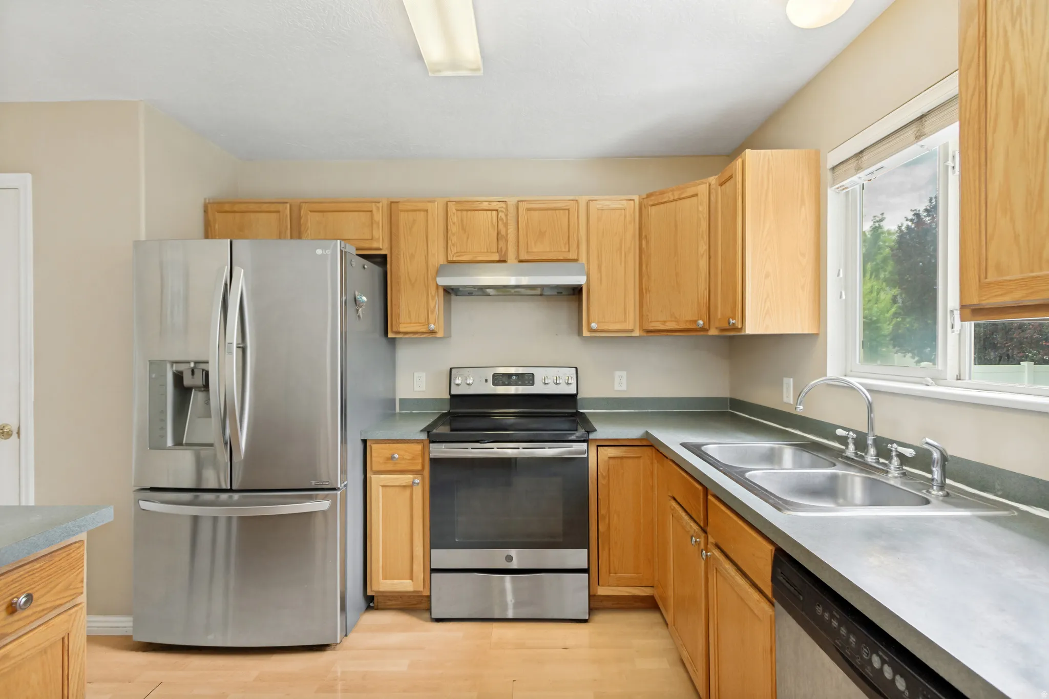 Kitchen featuring light wood cabinetry, stainless steel appliances, a double basin sink, and wood-finish flooring