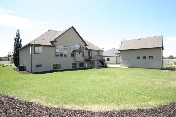 Expansive backyard featuring a manicured lawn, a multi-story residence with a stucco exterior, and a detached auxiliary building