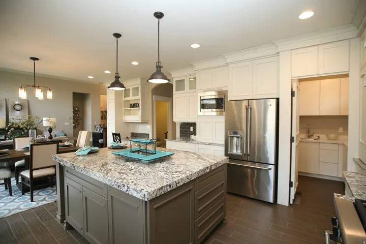 Spacious kitchen featuring a large central island with a granite-style countertop, pendant lighting, stainless steel appliances, white cabinetry, and wood-finish flooring