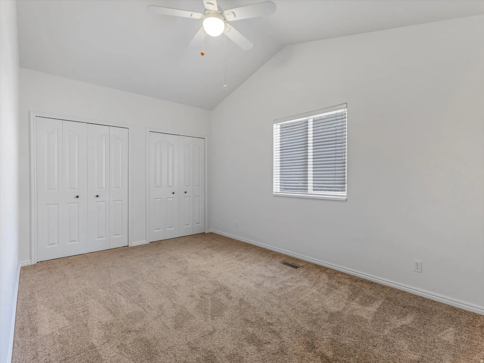 Bedroom 2-Vaulted ceiling bedroom featuring a ceiling fan with integrated lighting, two sets of bi-fold closet doors, a window with horizontal blinds, and neutral-tone carpeting