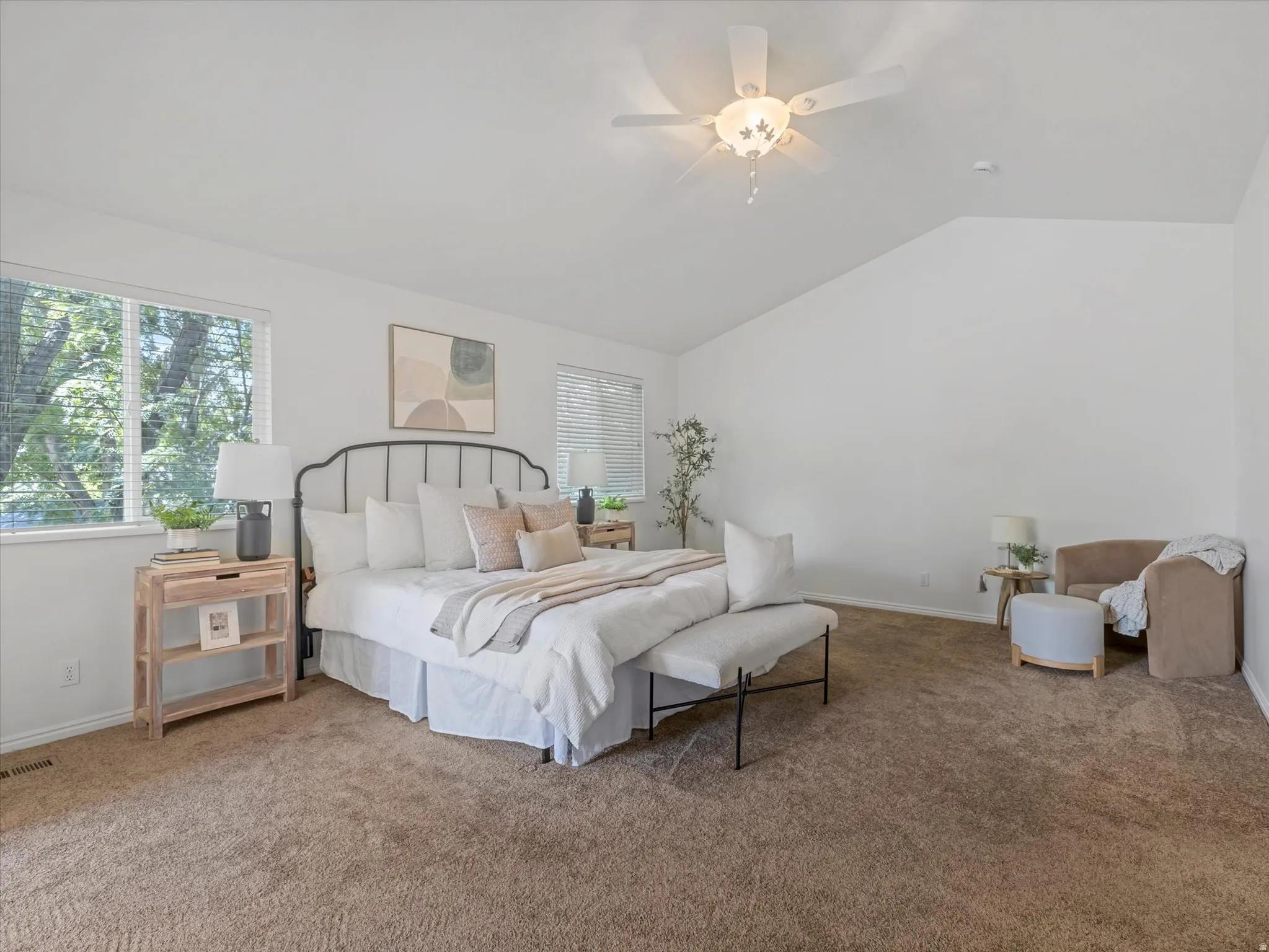 Spacious bedroom featuring neutral carpeting, a vaulted ceiling, and multiple windows with blinds