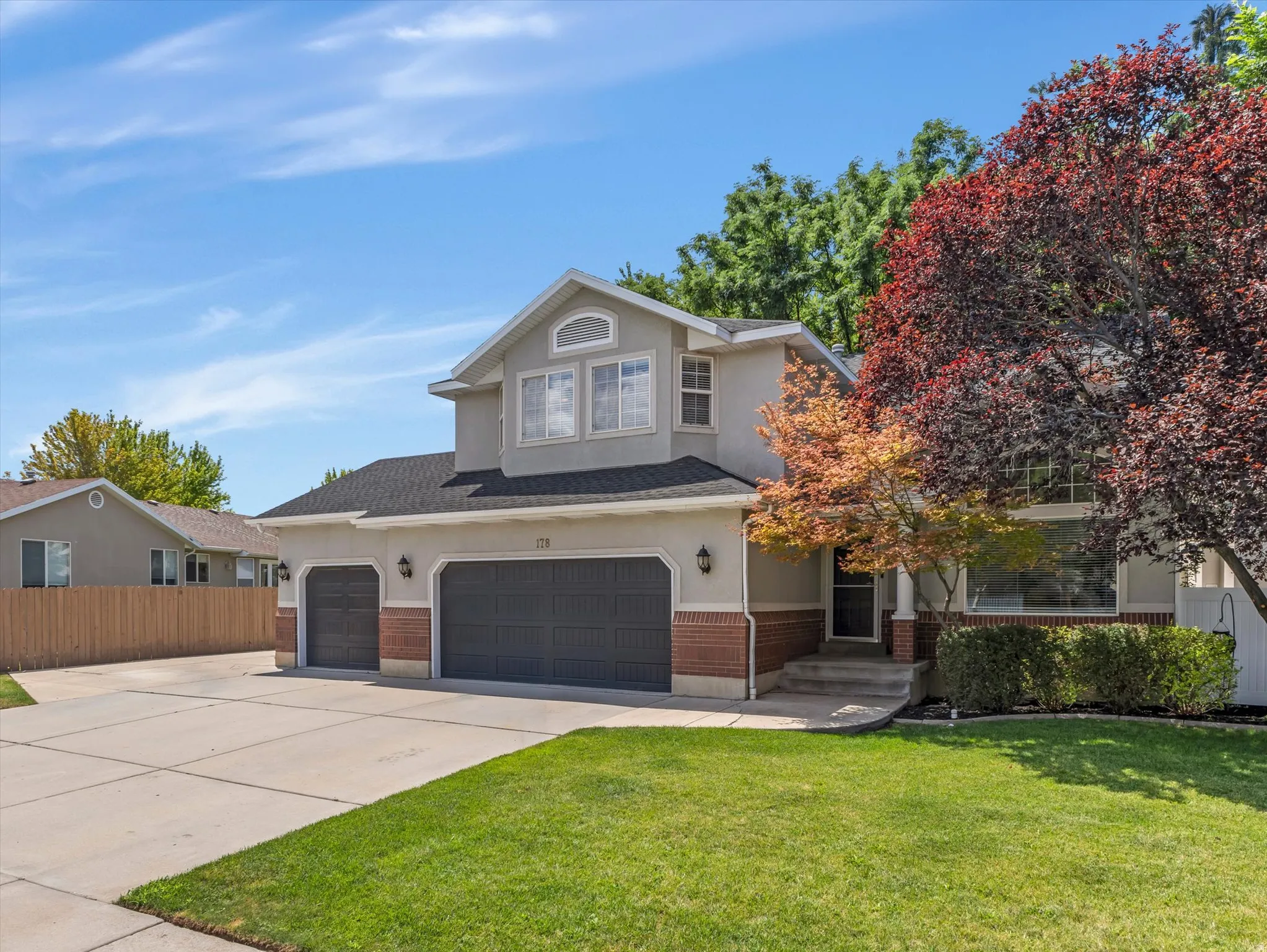Two-story stucco and brick exterior featuring a black shingle roof and a two-car garage