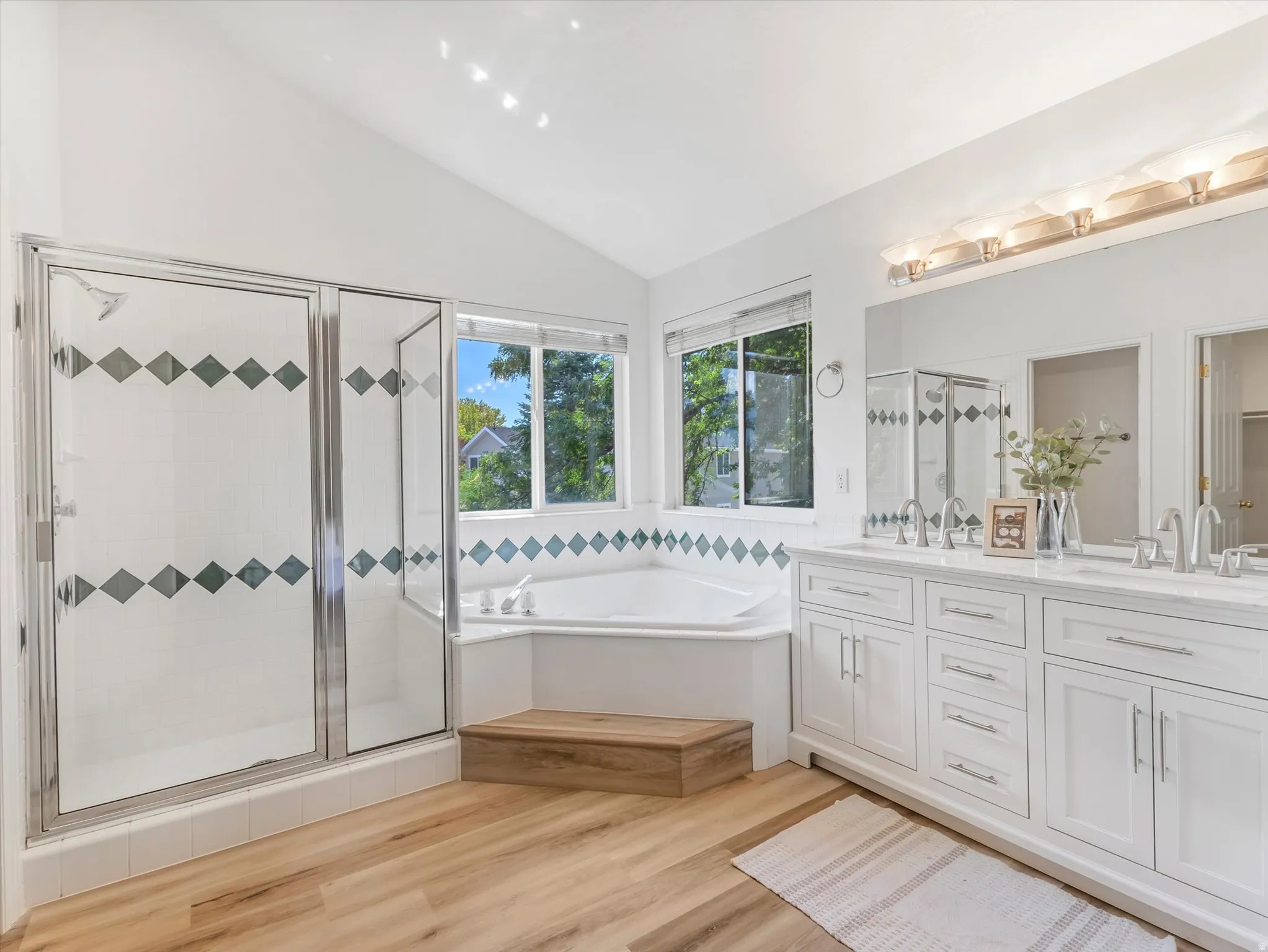 Bathroom featuring wood-finish flooring, a glass-enclosed shower, corner soaking tub, and a  new dual vanity with a large mirror
