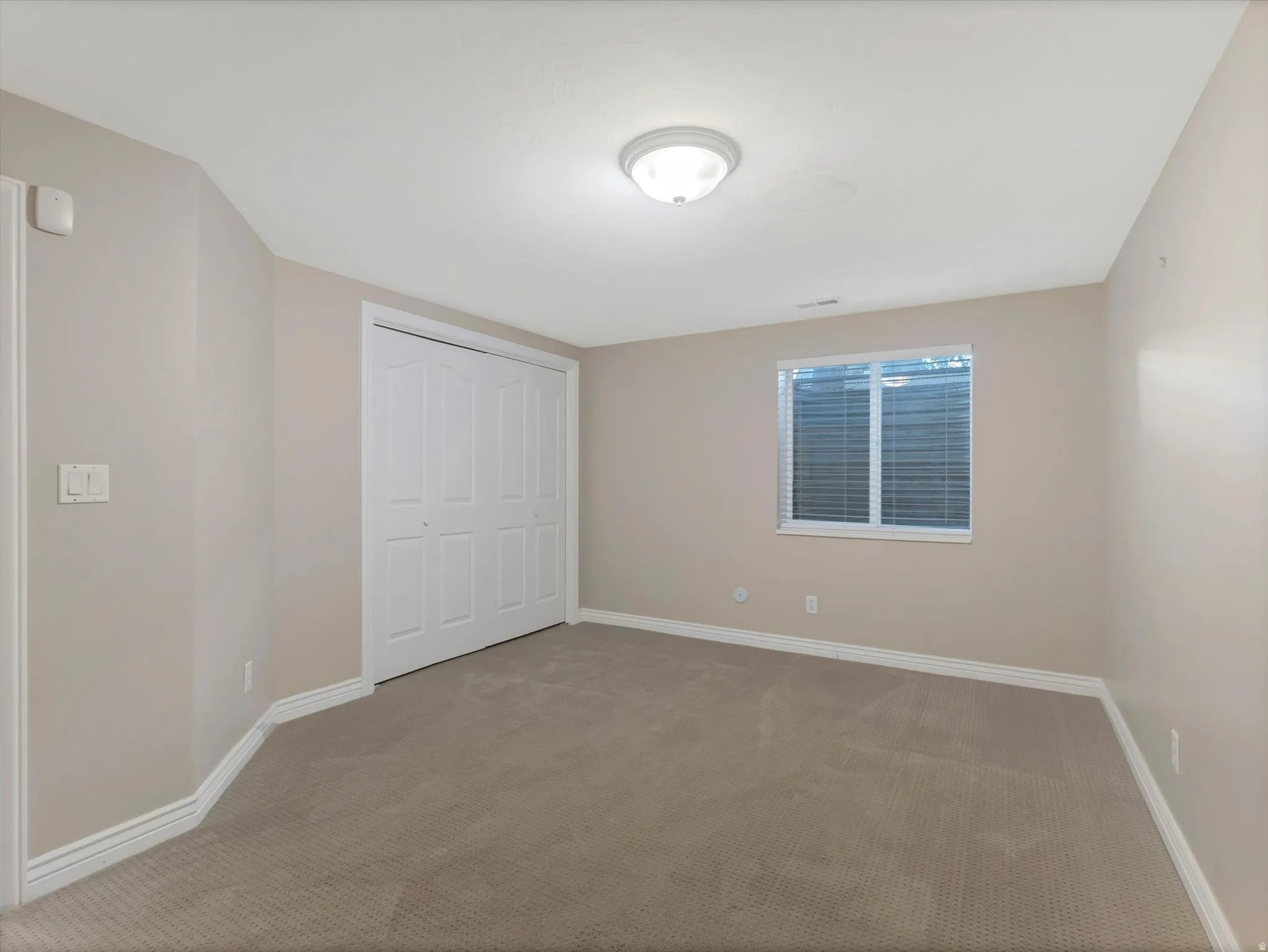 Bedroom 6-Carpeted room featuring a white bi-fold closet door, a single window with horizontal blinds, neutral wall paint, white baseboards, and a flush-mount ceiling light fixture