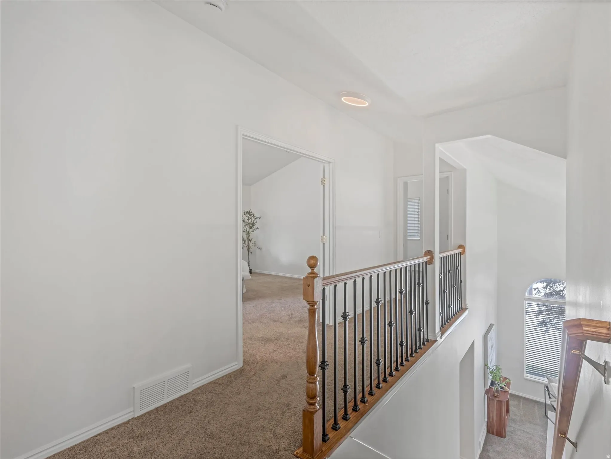 Staircase with wood newel posts and wrought iron balusters opening to a carpeted hallway