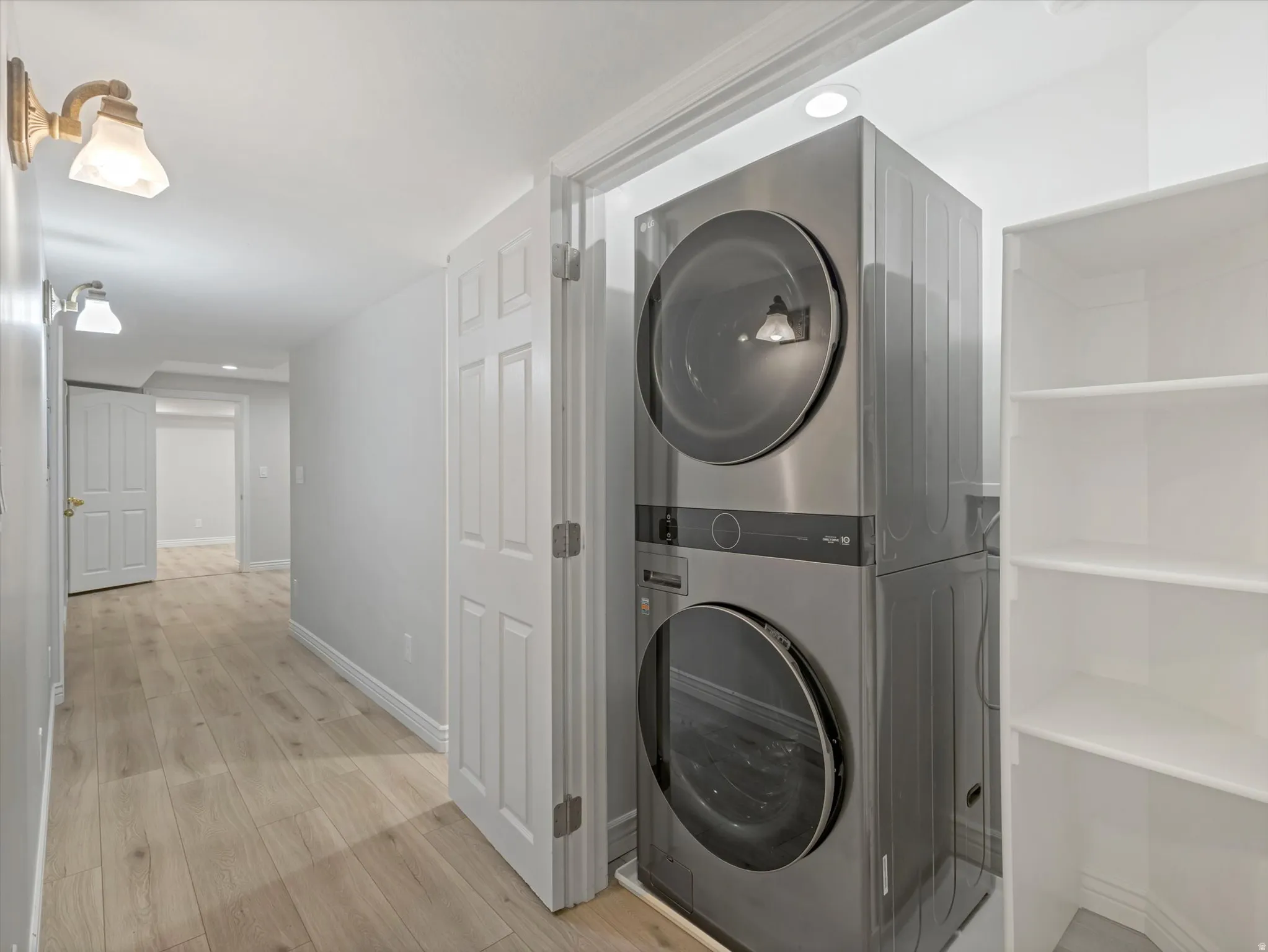 Dedicated laundry area featuring a stacked washer and dryer unit, white shelving, wood-finish flooring, recessed lighting, and a neutral wall color