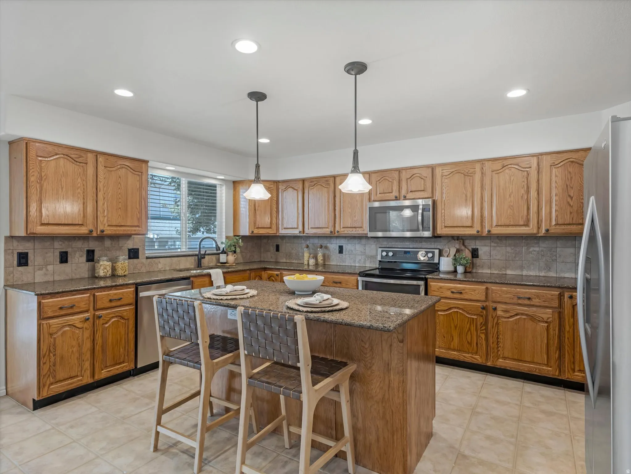 Kitchen featuring a central island with counter seating, granite countertops, wood cabinetry, stainless steel appliances, and recessed lighting