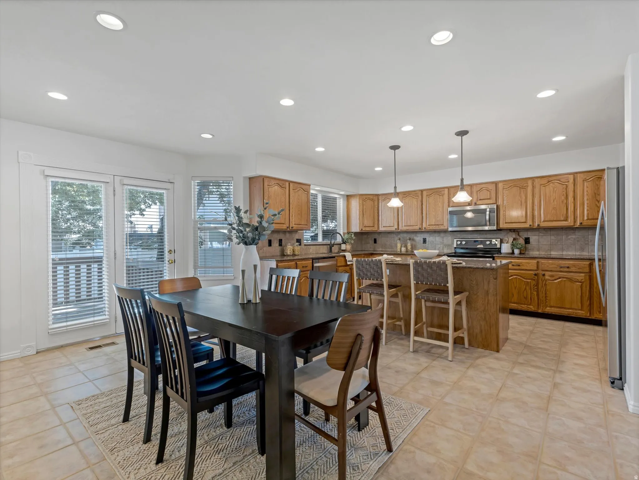Open-concept kitchen and dining area featuring warm wood cabinetry, stainless steel appliances, a kitchen island with pendant lighting, and tile flooring