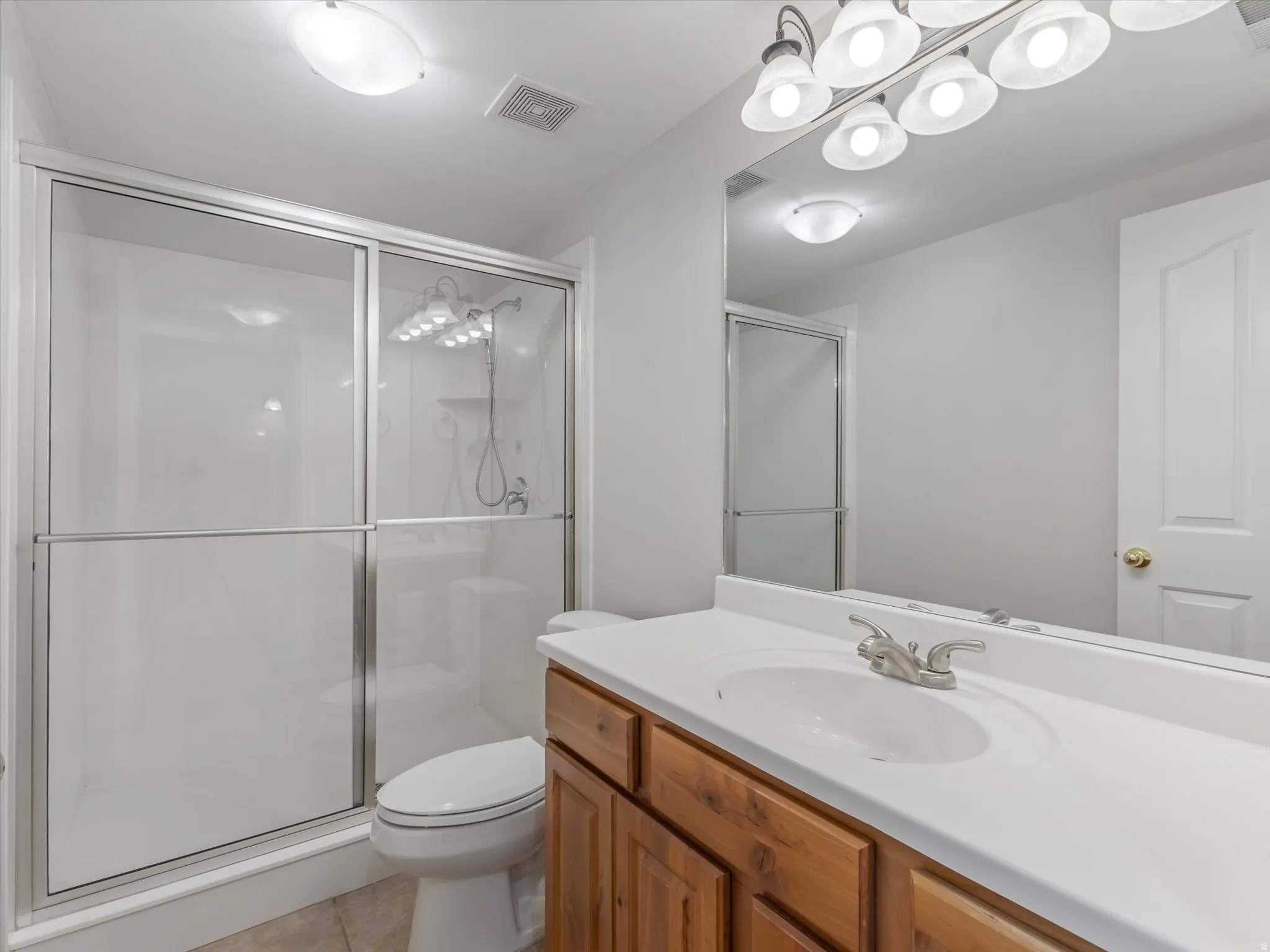 ADU Bathroom featuring a wood-finish vanity with an integrated sink and brushed nickel faucet, a large wall-mounted mirror, and a shower with sliding glass doors