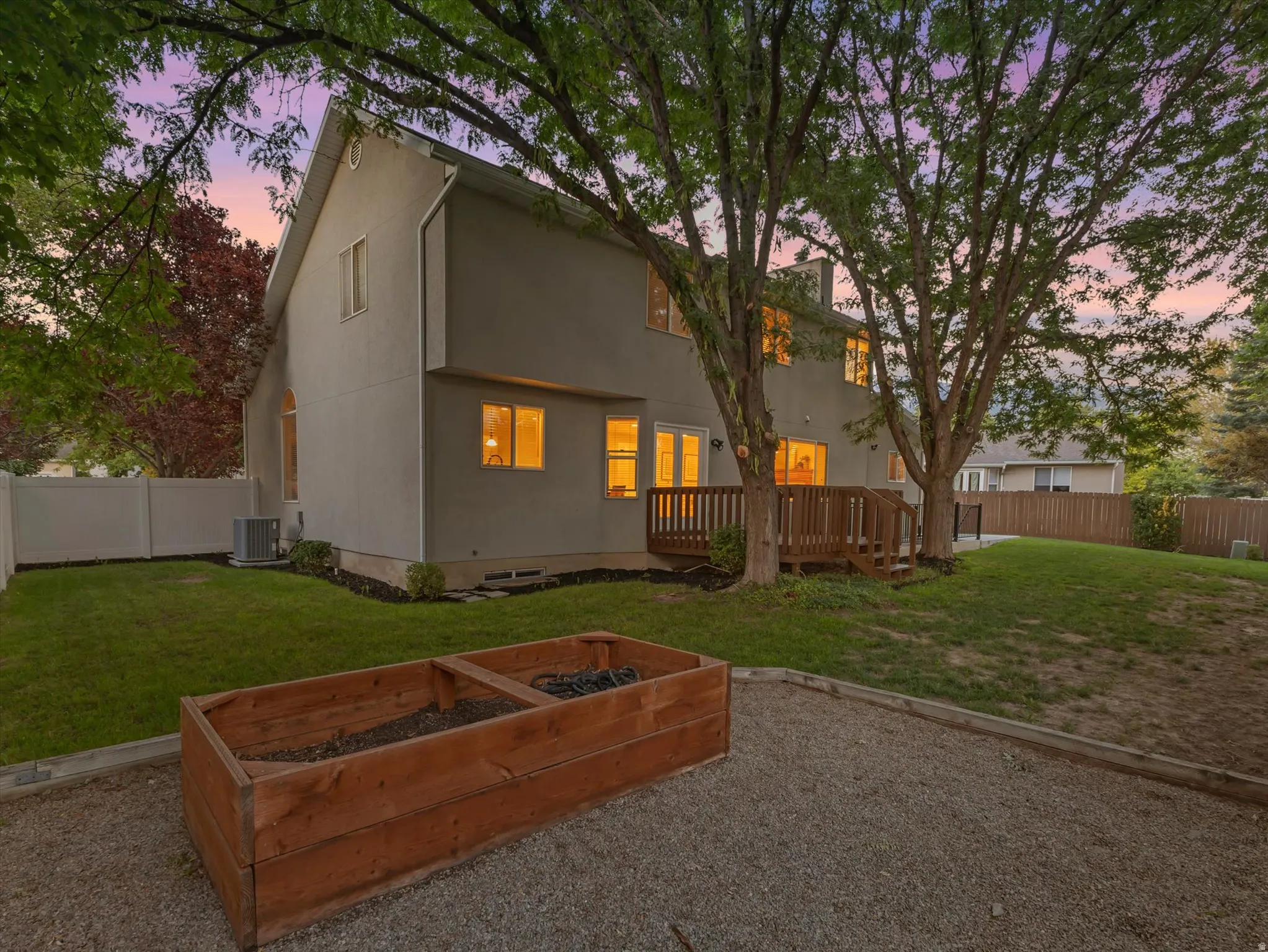 Expansive backyard featuring a wood deck with stairs, a gravel patio area, and a large wooden planter box