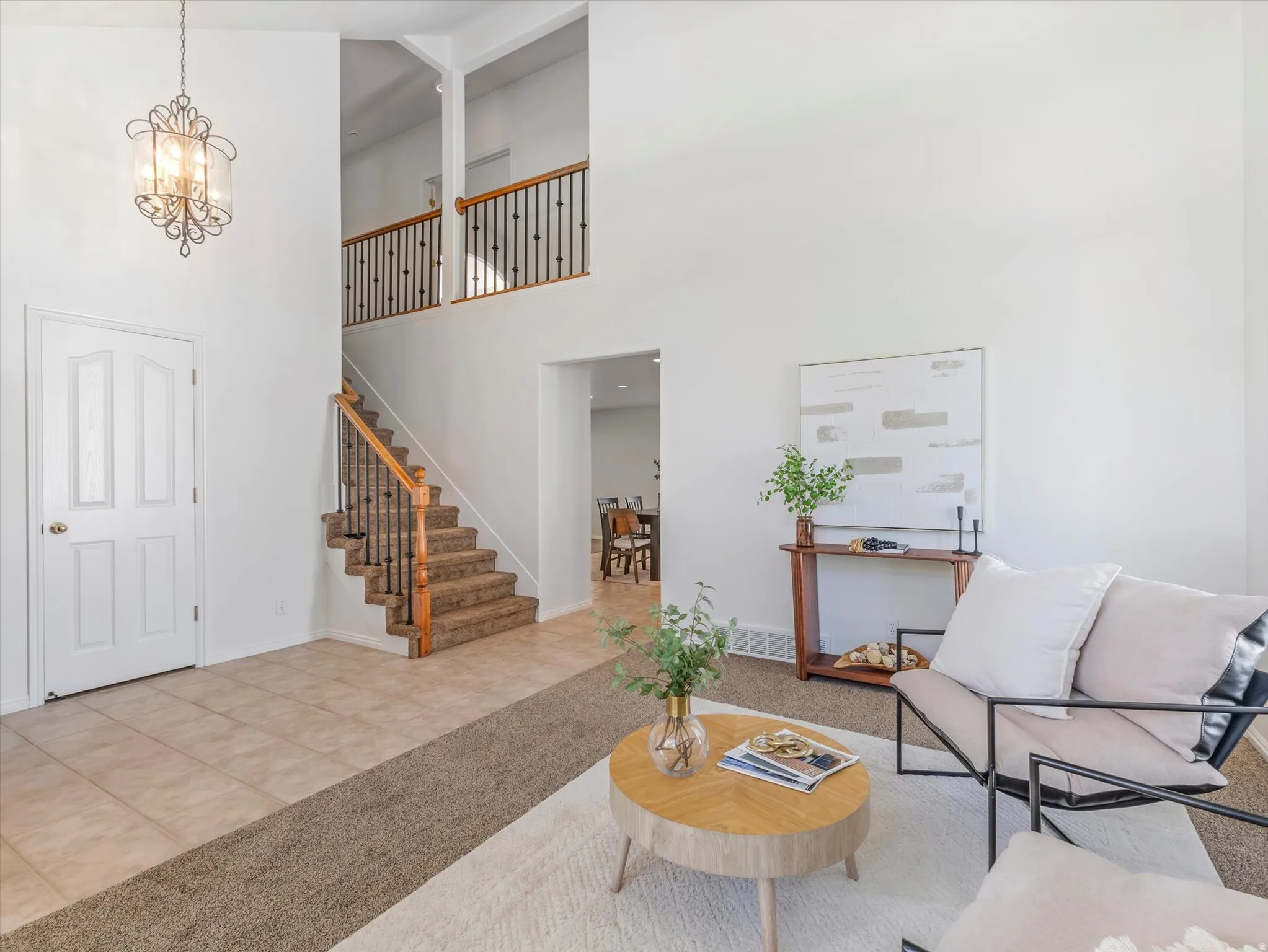 Two-story  bright foyer featuring an chandelier, a carpeted staircase with wood handrails and wrought iron balusters, and tile flooring