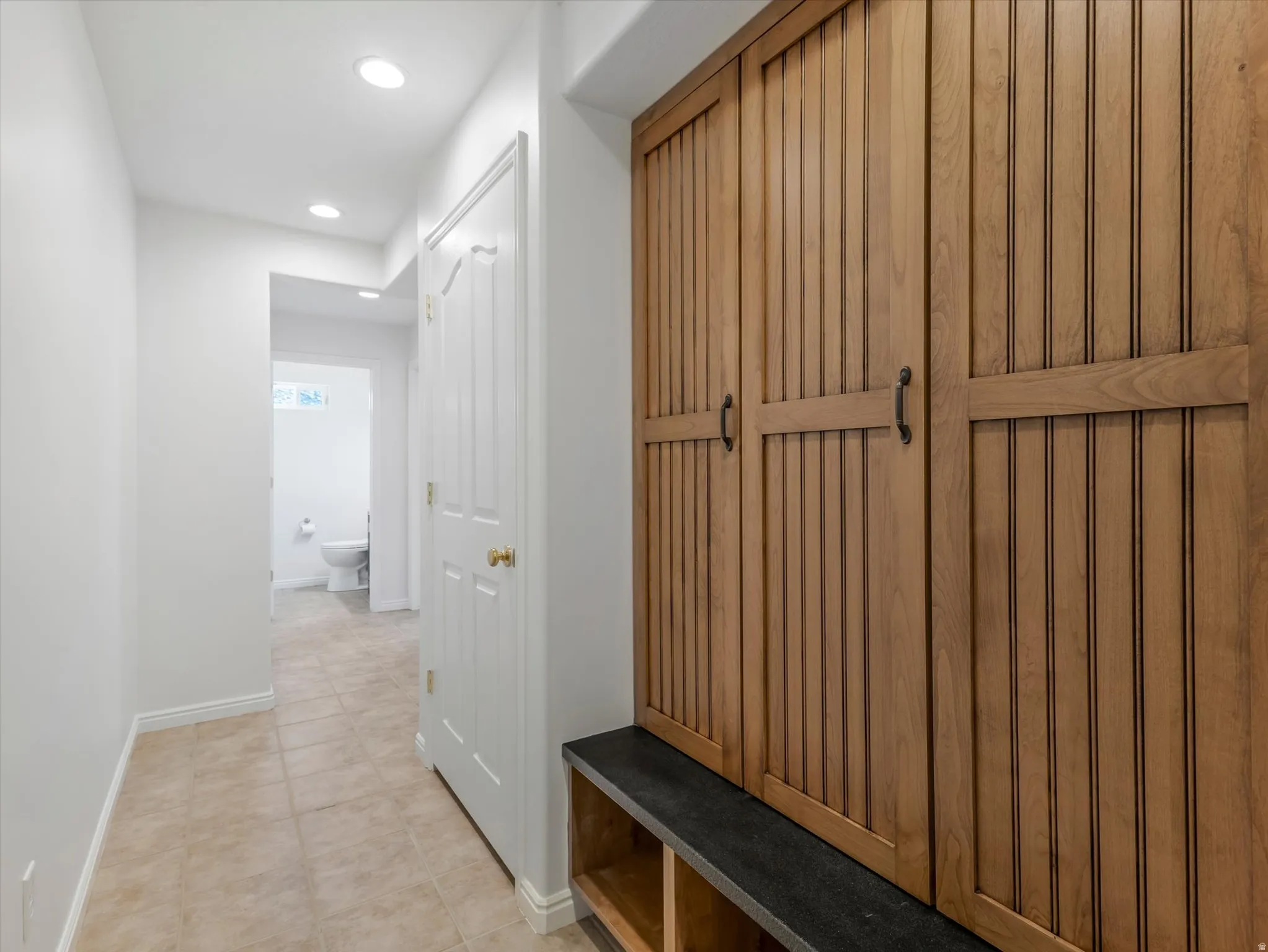 Built-in wood-finish storage unit with black hardware, integrated bench seating, and recessed lighting near garage entrance.