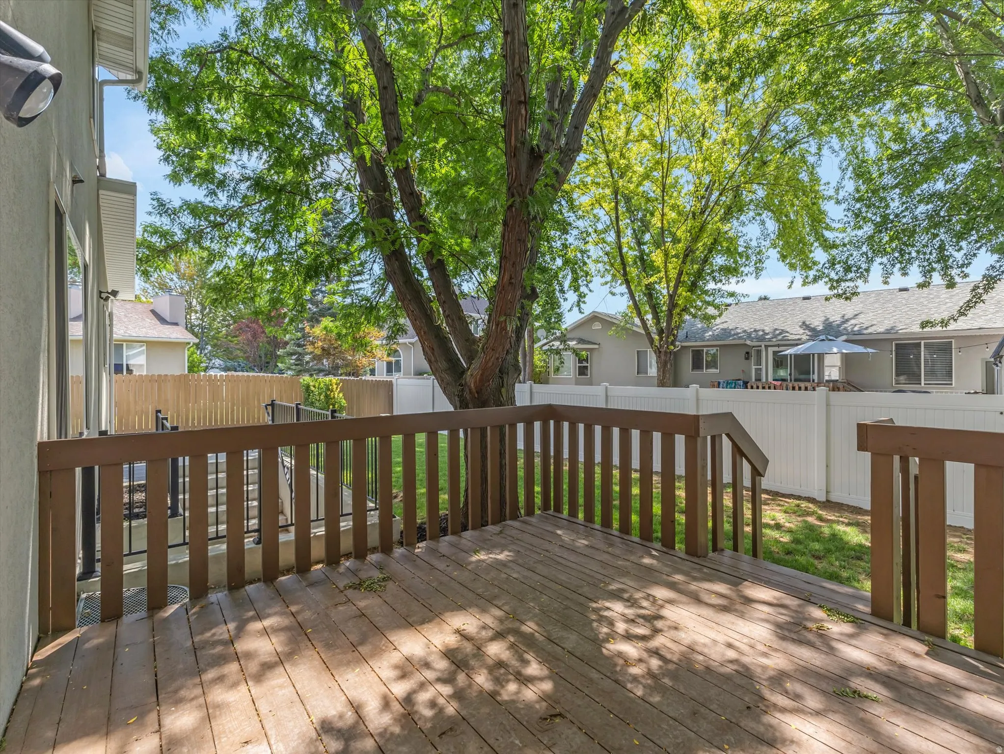 Wood-finish deck with a brown railing, overlooking a private yard with mature trees and a white privacy fence