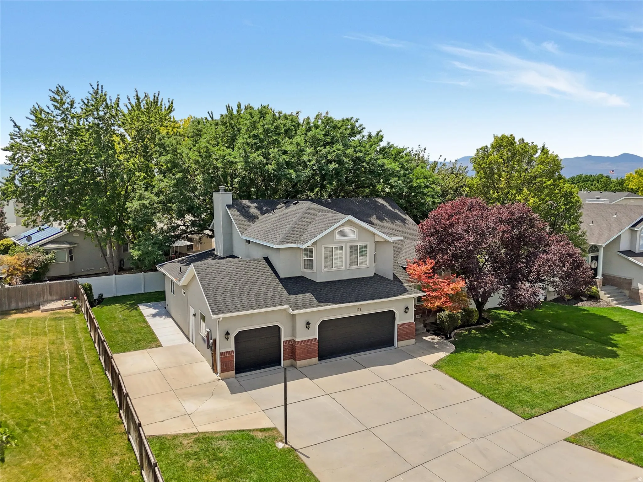 Two-story residence featuring a two-car garage, brick accents, and a front yard with mature trees