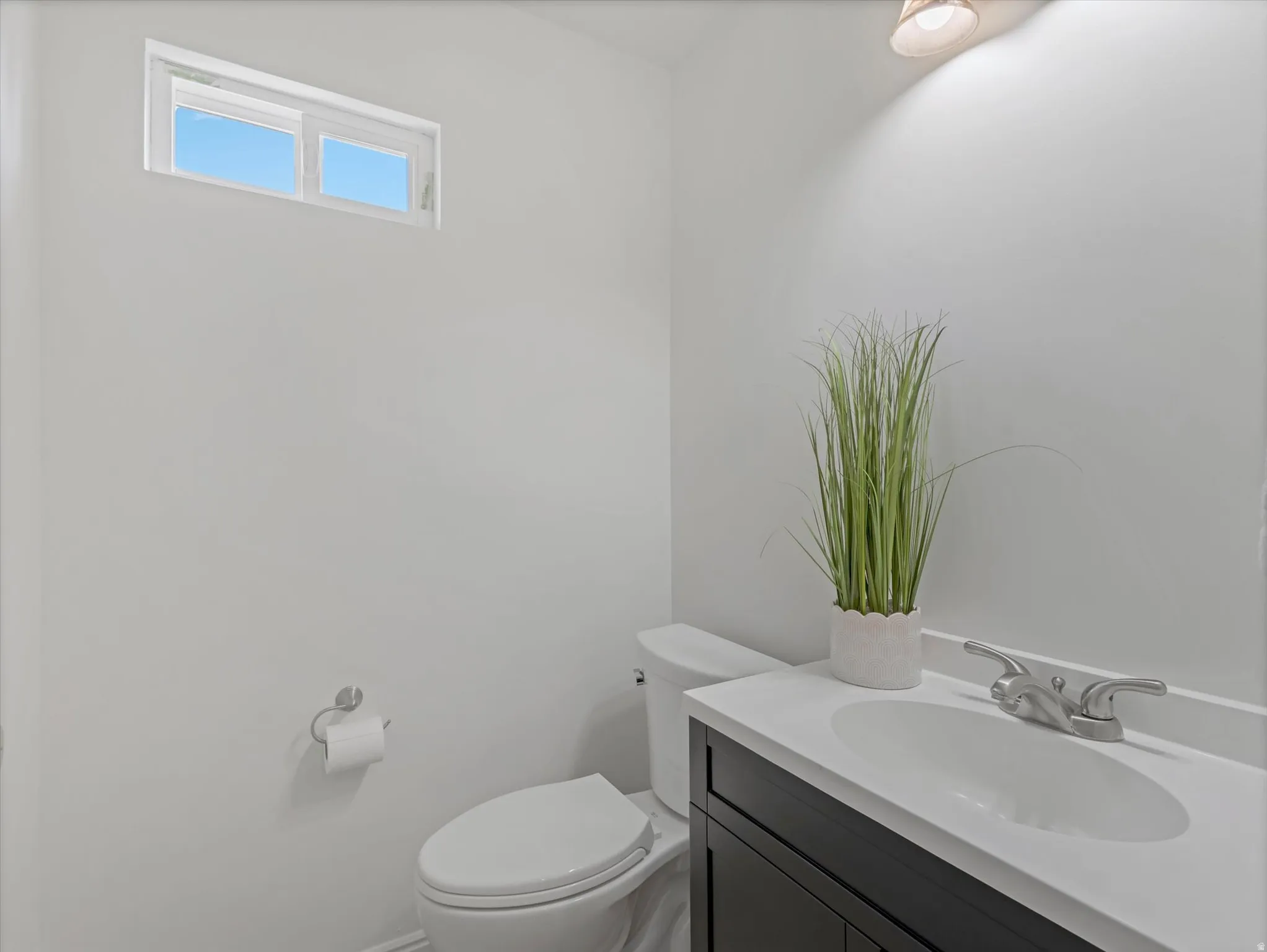 Powder room featuring a dark wood-finish vanity with an integrated white sink, brushed nickel faucet, and a horizontally oriented window