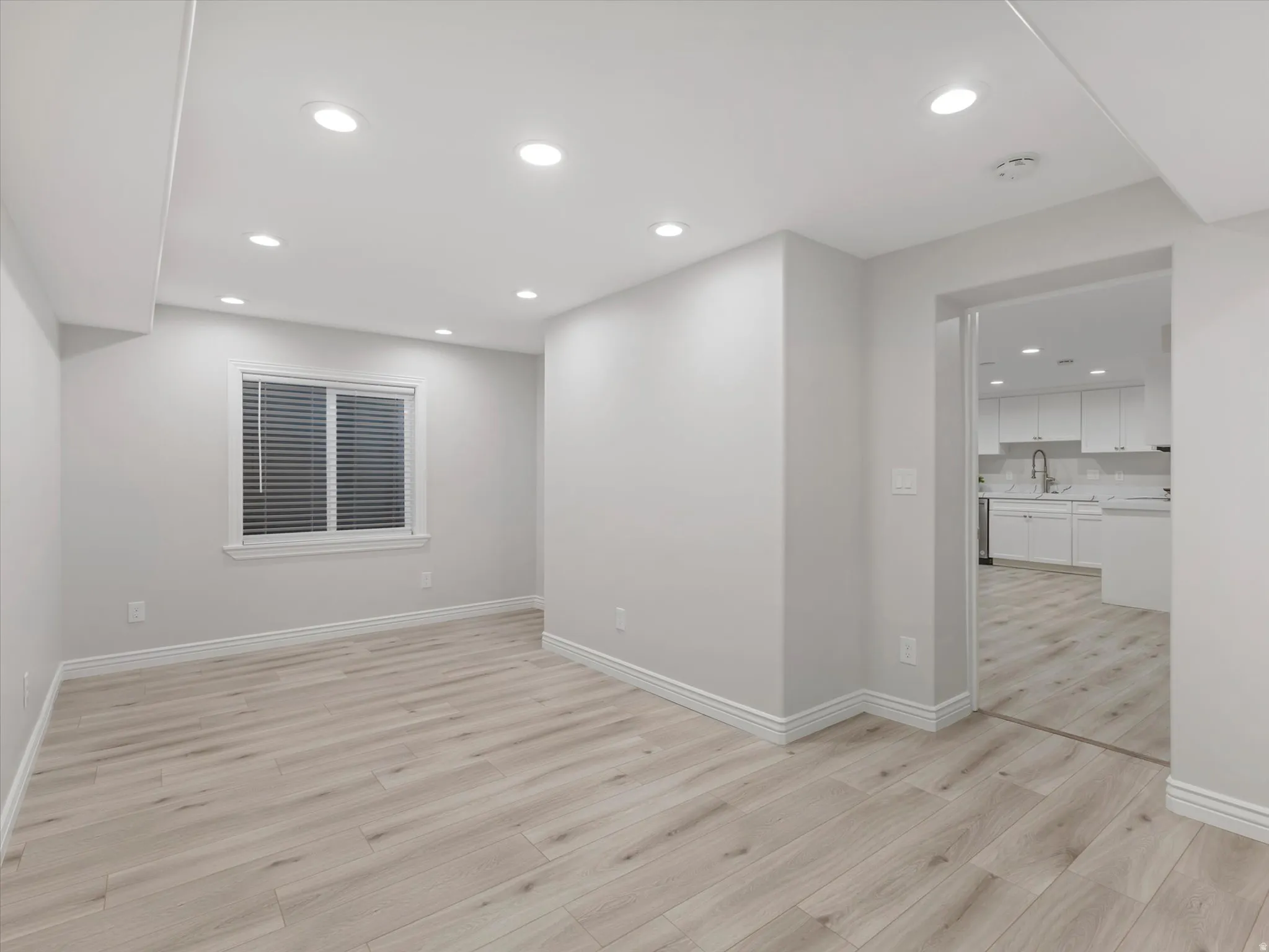 Spacious Basement ADU living room featuring light wood-finish flooring, recessed lighting, and a window with horizontal blinds