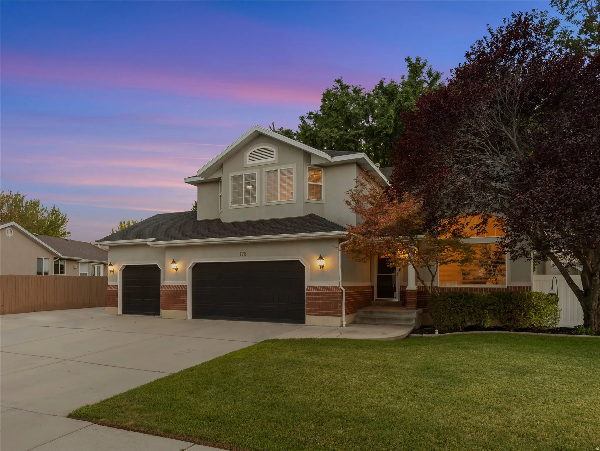Contemporary residence featuring a three-car garage with black doors, brick accents, and a light gray stucco exterior